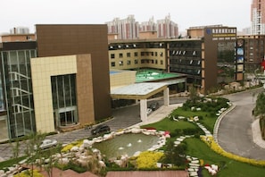 A hotel with a modern architectural design, featuring a covered outdoor area with a fountain, landscaped gardens, and a parking lot. - West International Trade Hotel (Beijing)