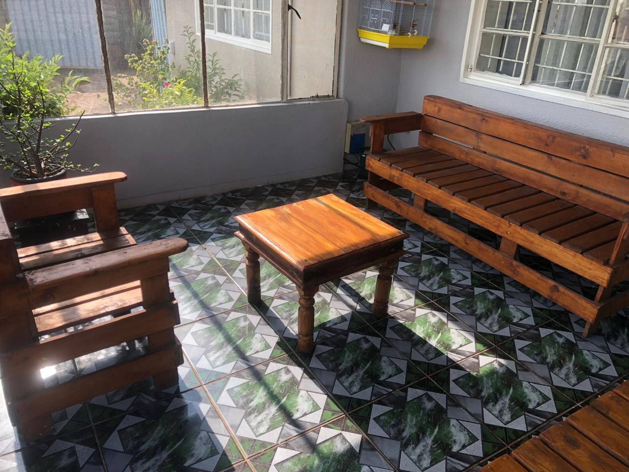 A patio with a wooden bench, a small table, and a potted plant.