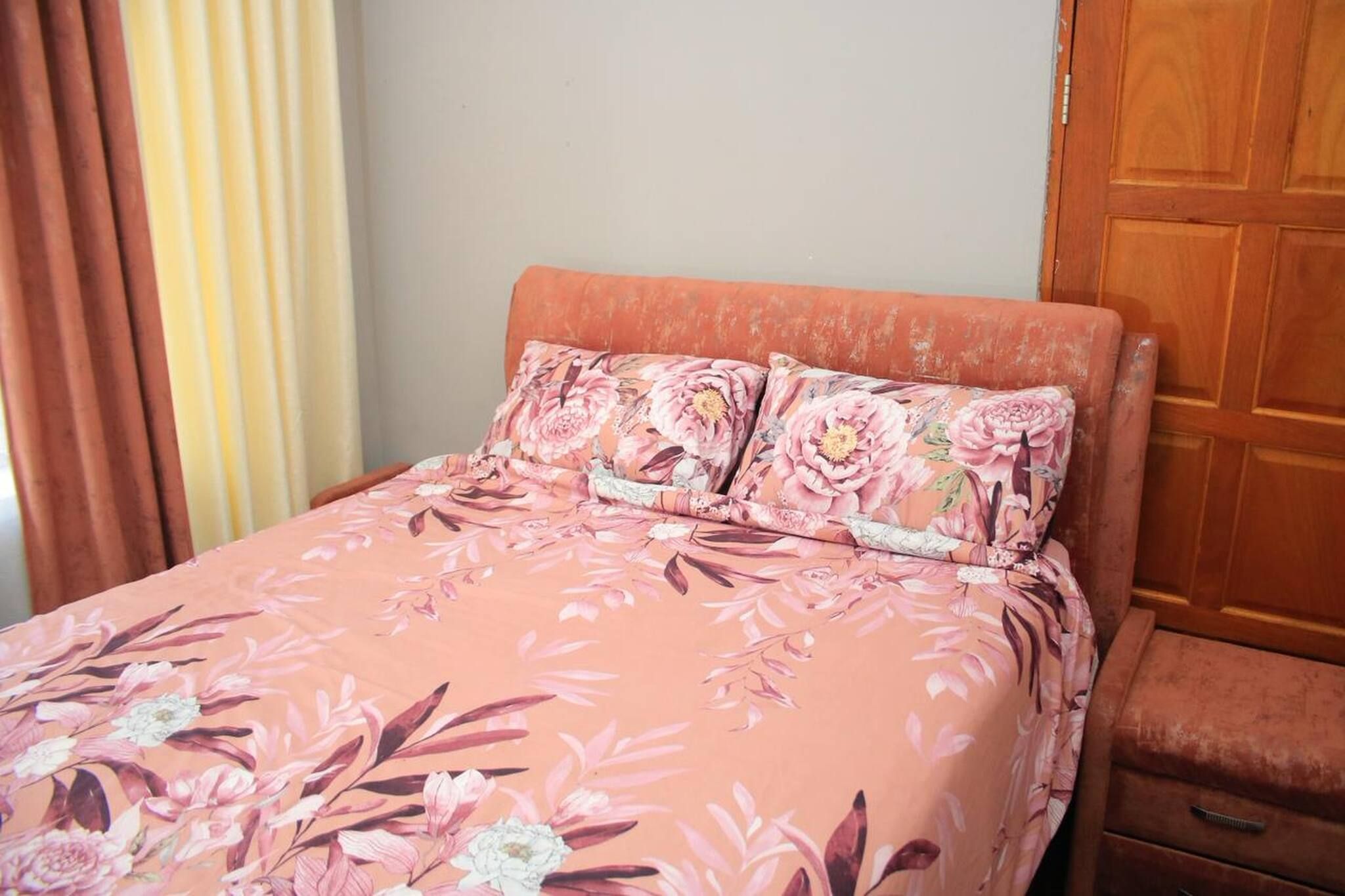A bed with floral bedding, a wooden nightstand, and a wooden wardrobe.