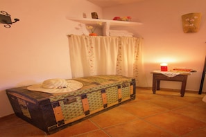 A small, cozy room with a bed, a table with a candle, and a shelf with decorative items. - Charming Countryside Home in Laroya (Laroya)