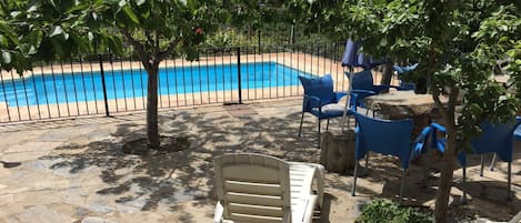 Una piscina rodeada por un patio de piedra, con sillas y sombrillas azules.