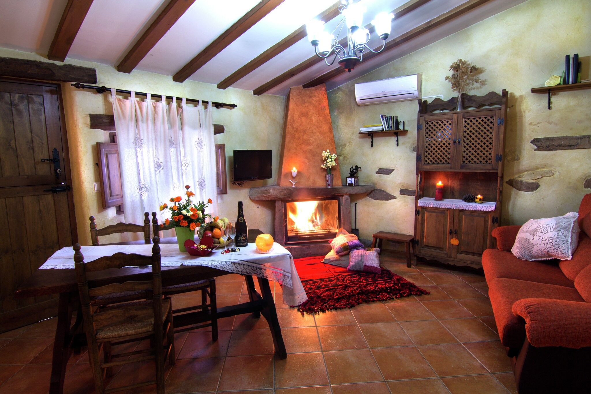 A cozy living room with a fireplace, wooden furniture, and a stone wall.