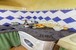 A kitchen with a washing machine, a coffee maker, a bottle of wine, and a fruit basket. - Luxurious Country Home in Laroya (Laroya)