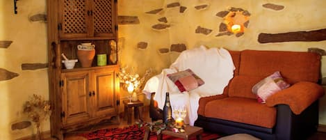 Una sala de estar acogedora con pared de piedra, un mueble de madera con cerámica, un tapiz rojo estampado y un sofá naranja cómodo.