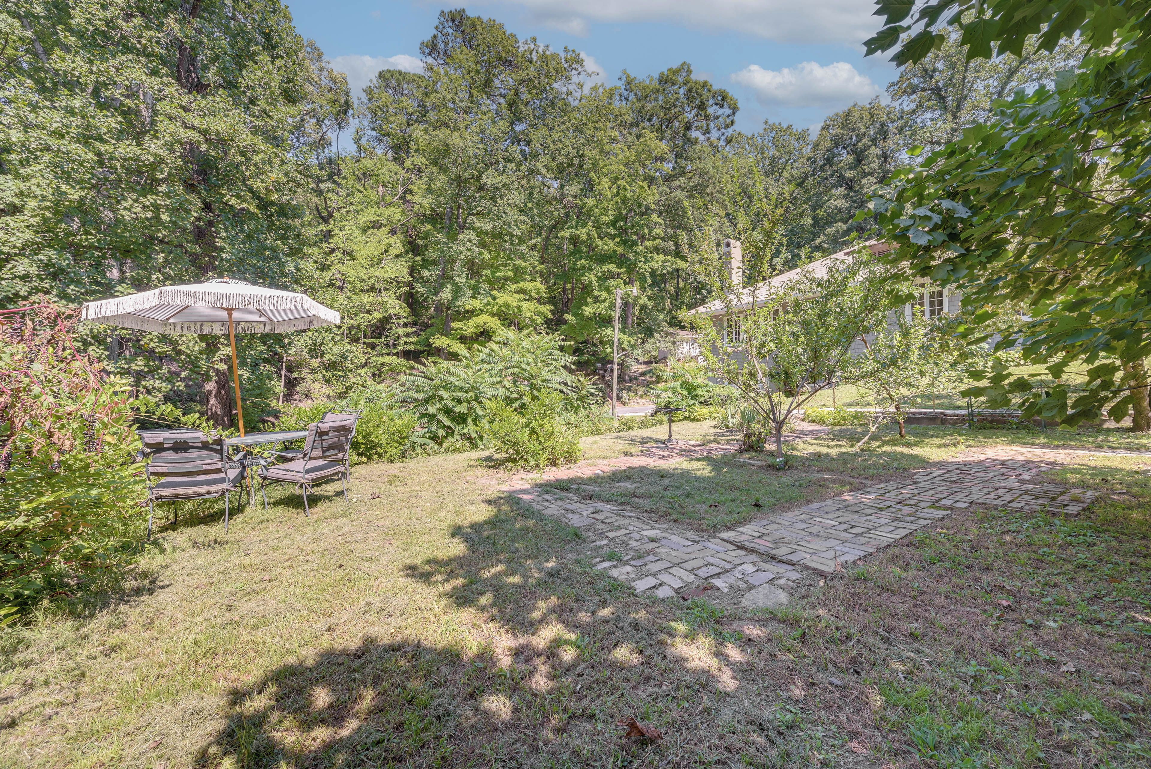 A garden with a patio table and chairs, surrounded by trees and a brick pathway.