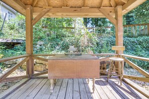 Um gazebo de madeira com mesa e cadeiras, rodeado por vegetação.