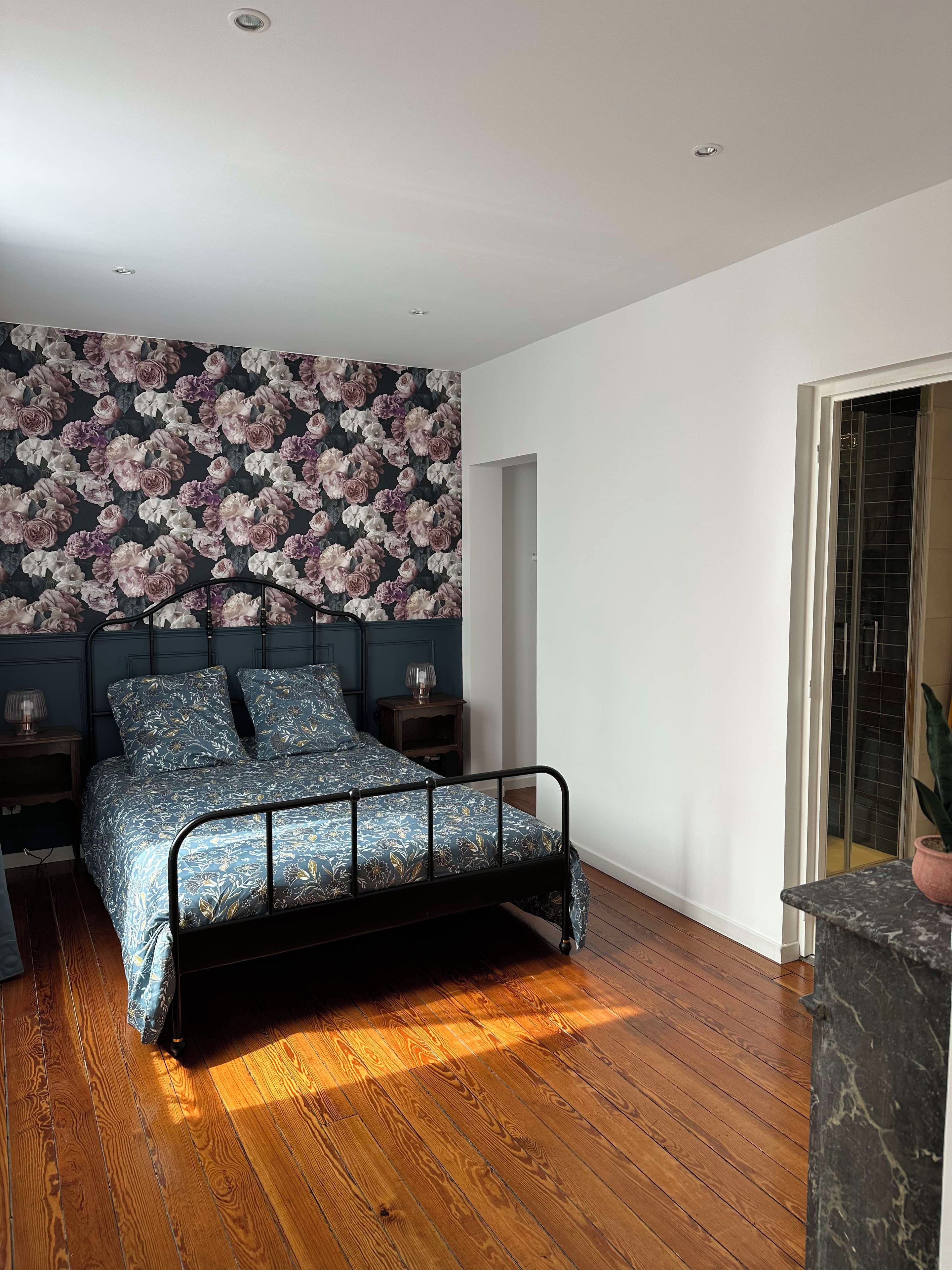 Een slaapkamer met een bed, nachtkastjes, bloemenbehang, een houten vloer en een uitzicht door een deur.
