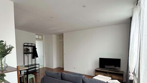 Una sala de estar moderna con un sofá gris, suelo de madera, un televisor y un comedor con una pequeña mesa y sillas.