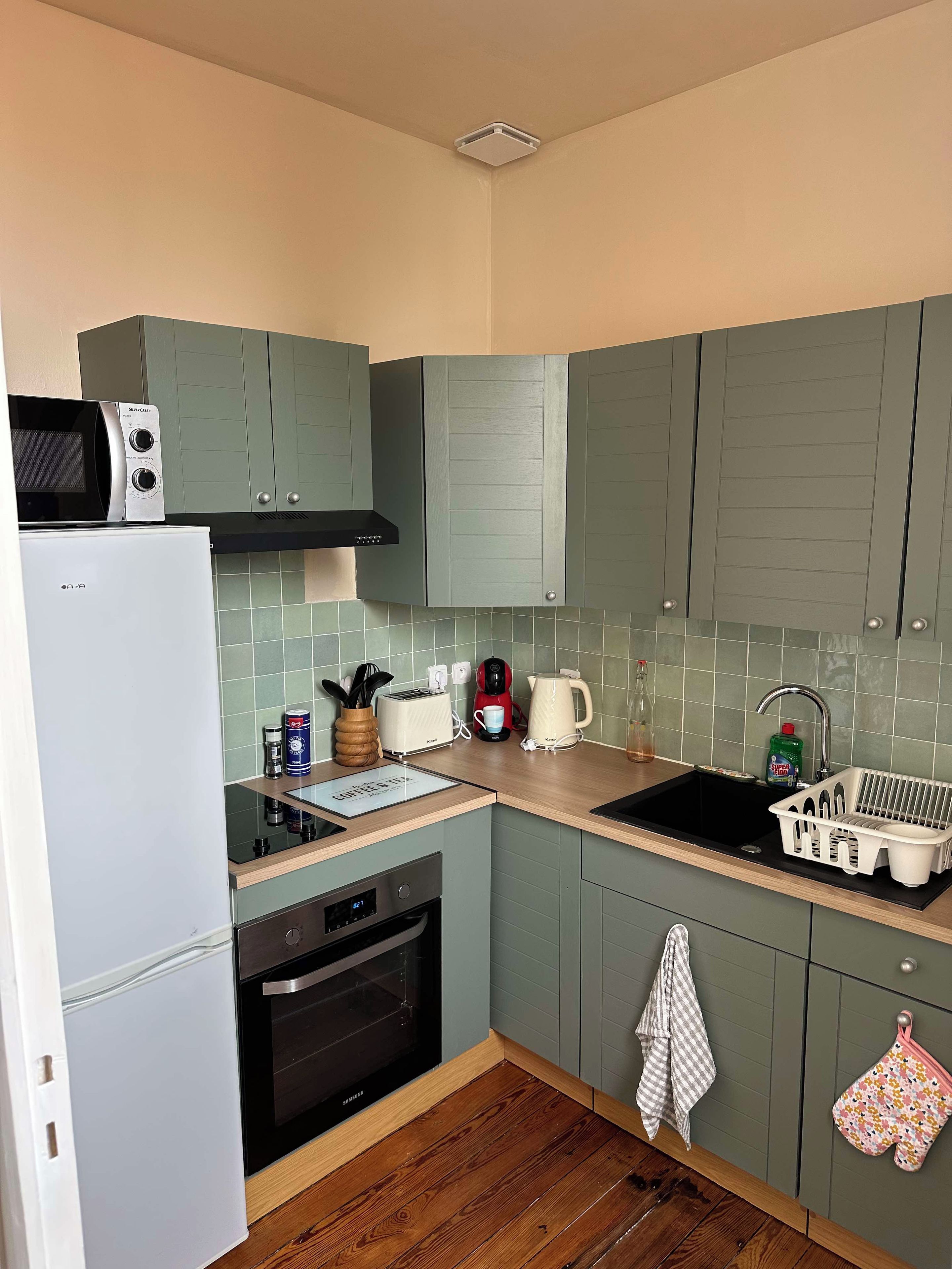 A compact kitchen with a microwave, toaster, kettle, and sink.