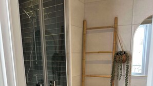 Un baño con cabina de ducha de vidrio, una escalera de madera, una toalla texturizada de color amarillo y un lavamanos blanco con espejo.