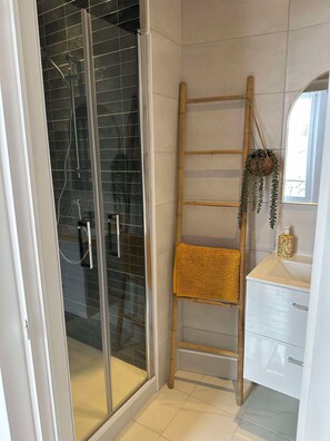 Un baño con cabina de ducha de vidrio, una escalera de madera, una toalla texturizada de color amarillo y un lavamanos blanco con espejo.