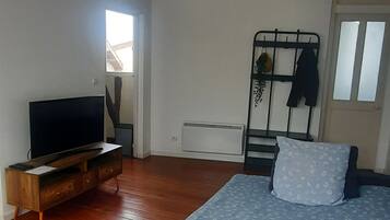 Een slaapkamer met een bed, een televisie op een houten standaard, een radiator en een raam met zonwering.