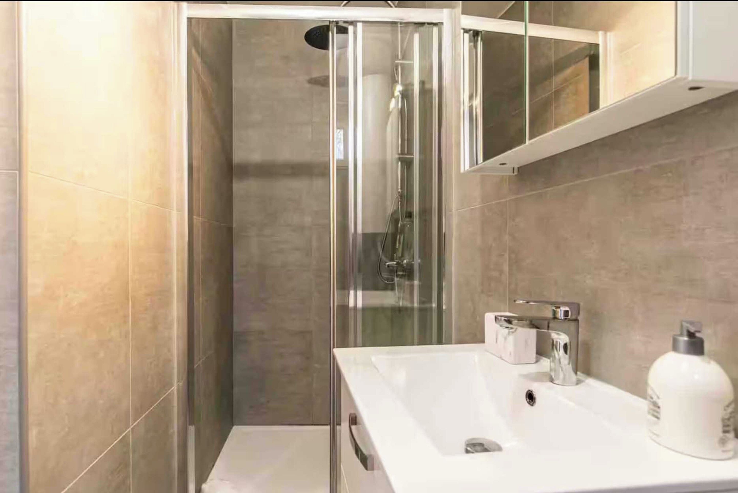 Ein modernes Badezimmer mit einer gläsernen Duschkabine, einem weißen Waschbecken und einem Spiegel darüber.
