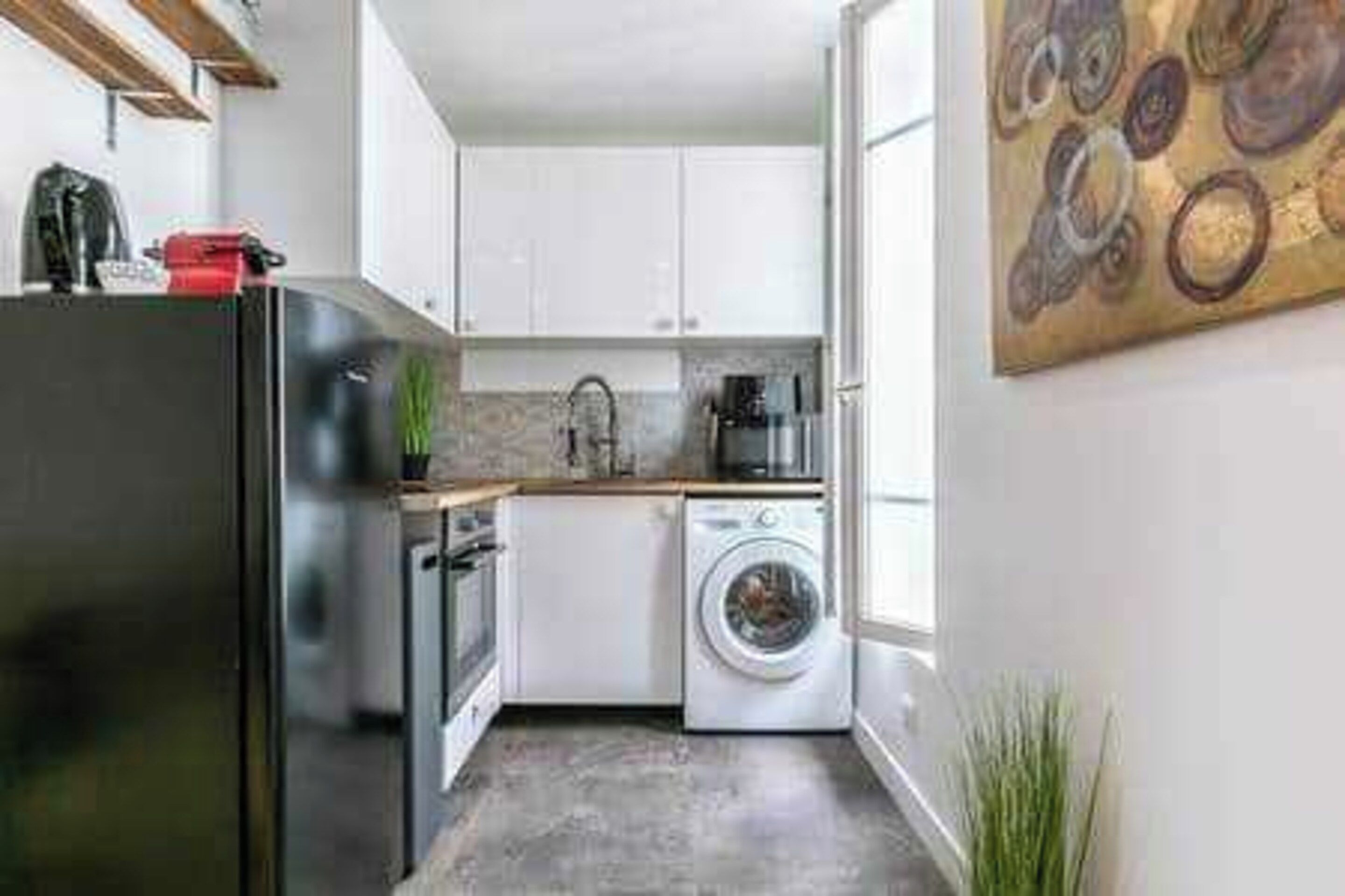 A compact kitchen with a refrigerator, oven, washing machine, and a sink.