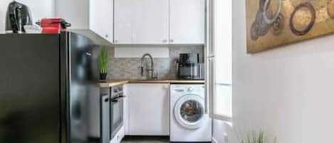 Una cocina compacta con refrigerador, horno, lavadora y pileta.