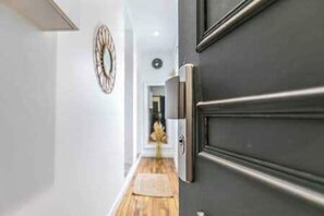 A hallway with a dark door, a clock on the wall, and a plant in the distance. - Charming Apartment - 2ch/6p - Montreuil (Montreuil)