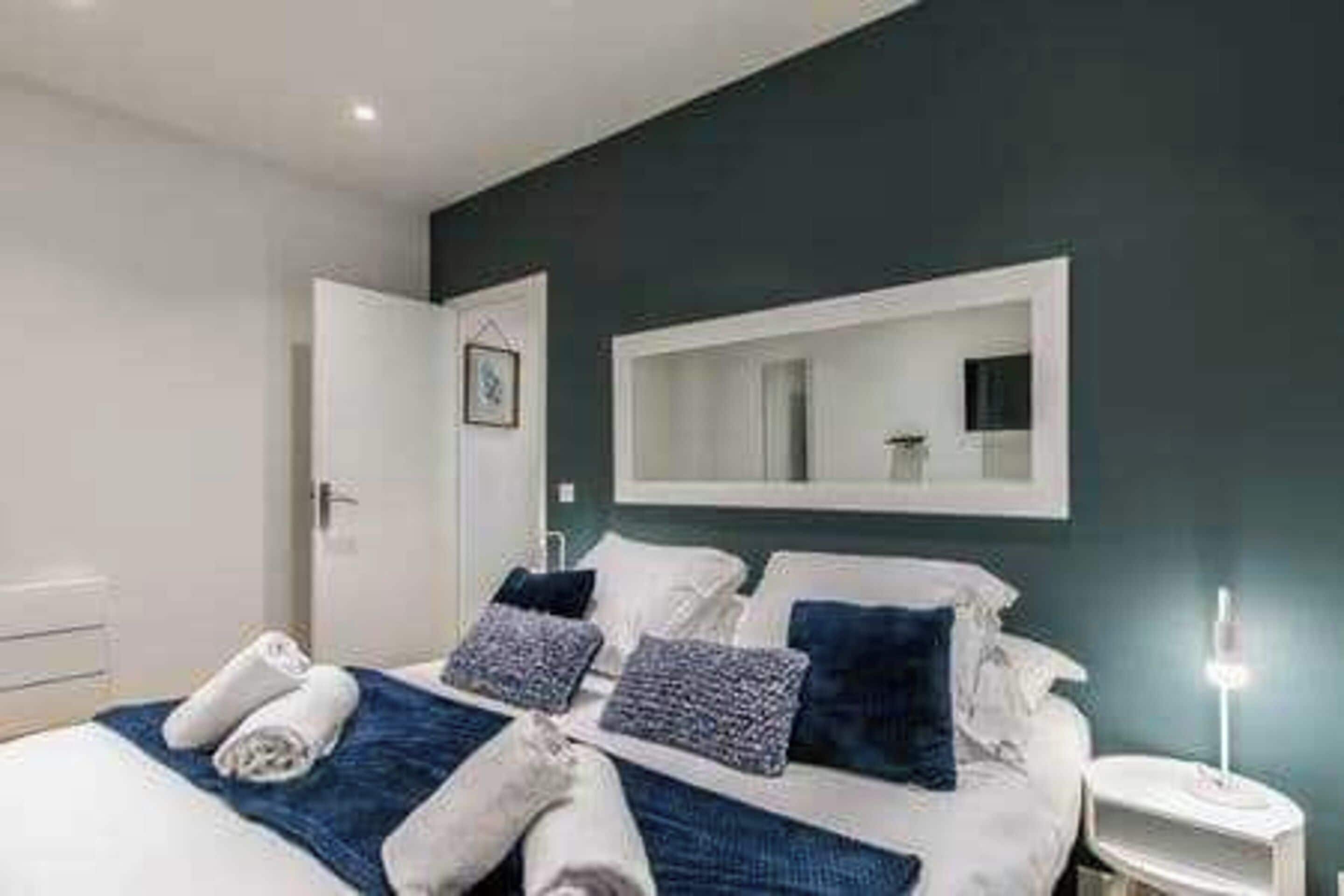 A hotel room with a bed, a bedside table, a nightstand, a mirror, and a door.