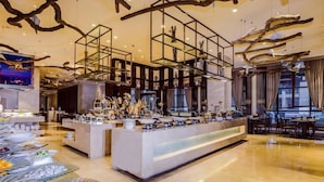Un área de bufé con una variedad de alimentos, un mostrador central de servicio y una decoración moderna con techos a la vista e iluminación.