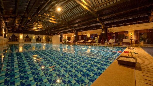 Una piscina interior con suelo de baldosas de ajedrez, sillas de descanso y una zona de terraza de madera.