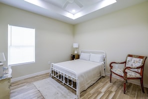 A bedroom with a bed, a chair, a nightstand, a lamp, and a window.
