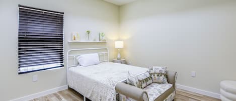 A bedroom with a bed, bedside table, lamp, and a window with blinds.