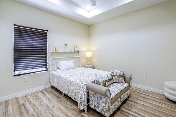 A bedroom with a bed, bedside table, lamp, and a window with blinds.