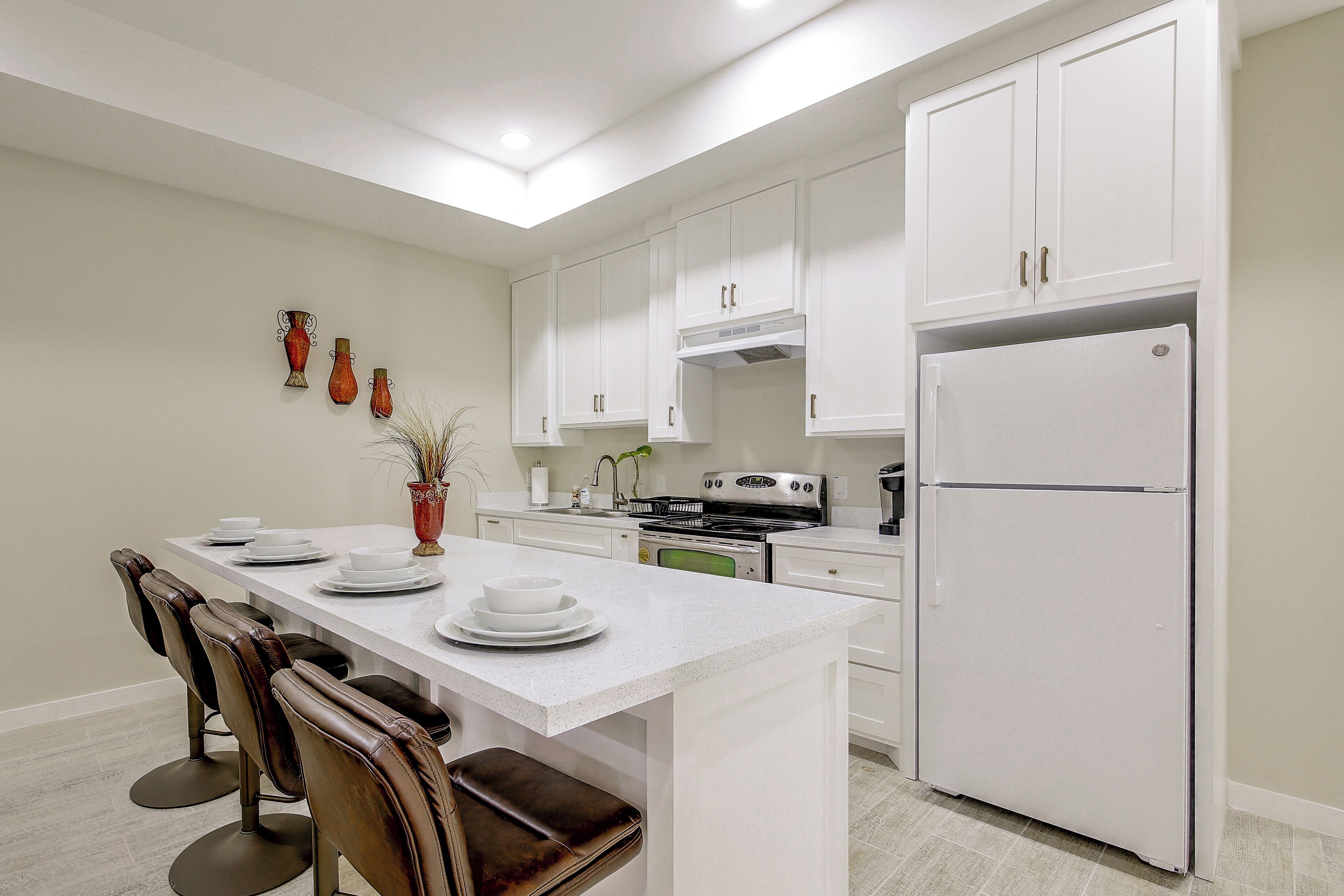 Una cocina moderna con armarios blancos, una isla central con asientos y un refrigerador de acero inoxidable.