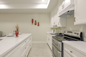 A modern kitchen with white cabinetry, a stainless steel stove, and a countertop with a vase of dried plants.