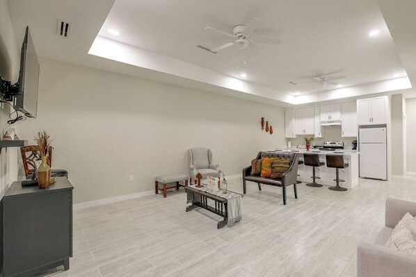 A spacious living area with a dining set, a sofa, a coffee table, and a kitchen area with a refrigerator and a stove.
