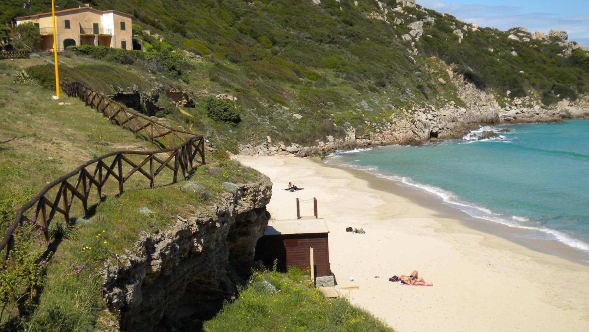 Une plage côtière avec un escalier en bois menant à un bâtiment, une plage de sable et une falaise rocheuse.