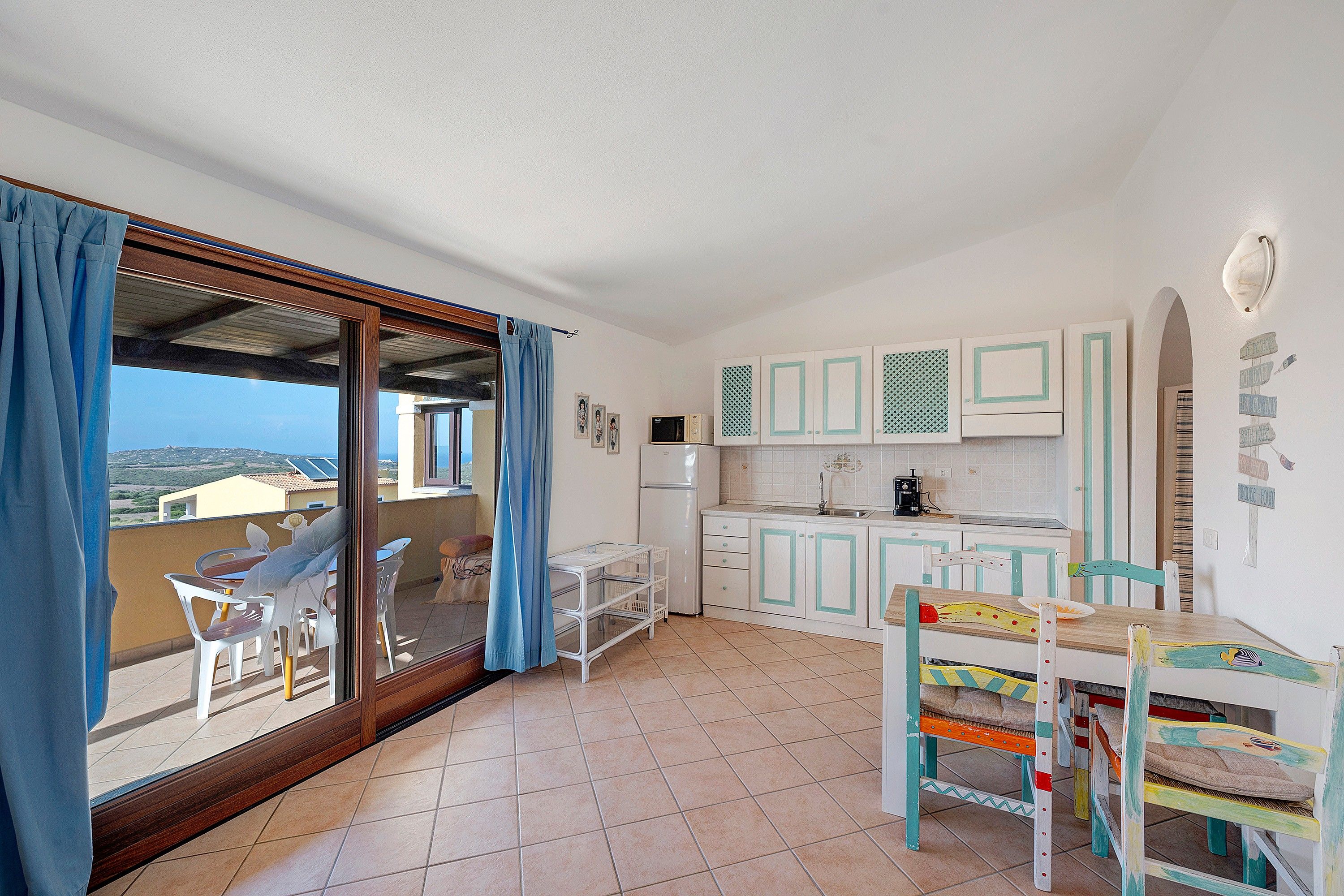 Ein Zimmer mit Balkon, einer Küche mit weißen Schränken und einer Essecke mit Tisch und Stühlen.