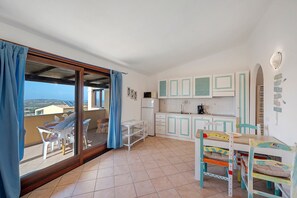 Una habitación con balcón, cocina con armarios blancos y comedor con mesa y sillas.
