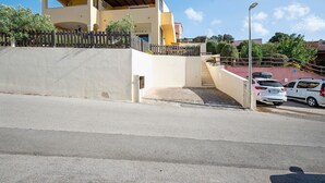 Un bâtiment à deux étages, doté d’un toit plat, d’une clôture en bois et d’une allée pavée menant à un espace de stationnement où se trouvent des voitures.