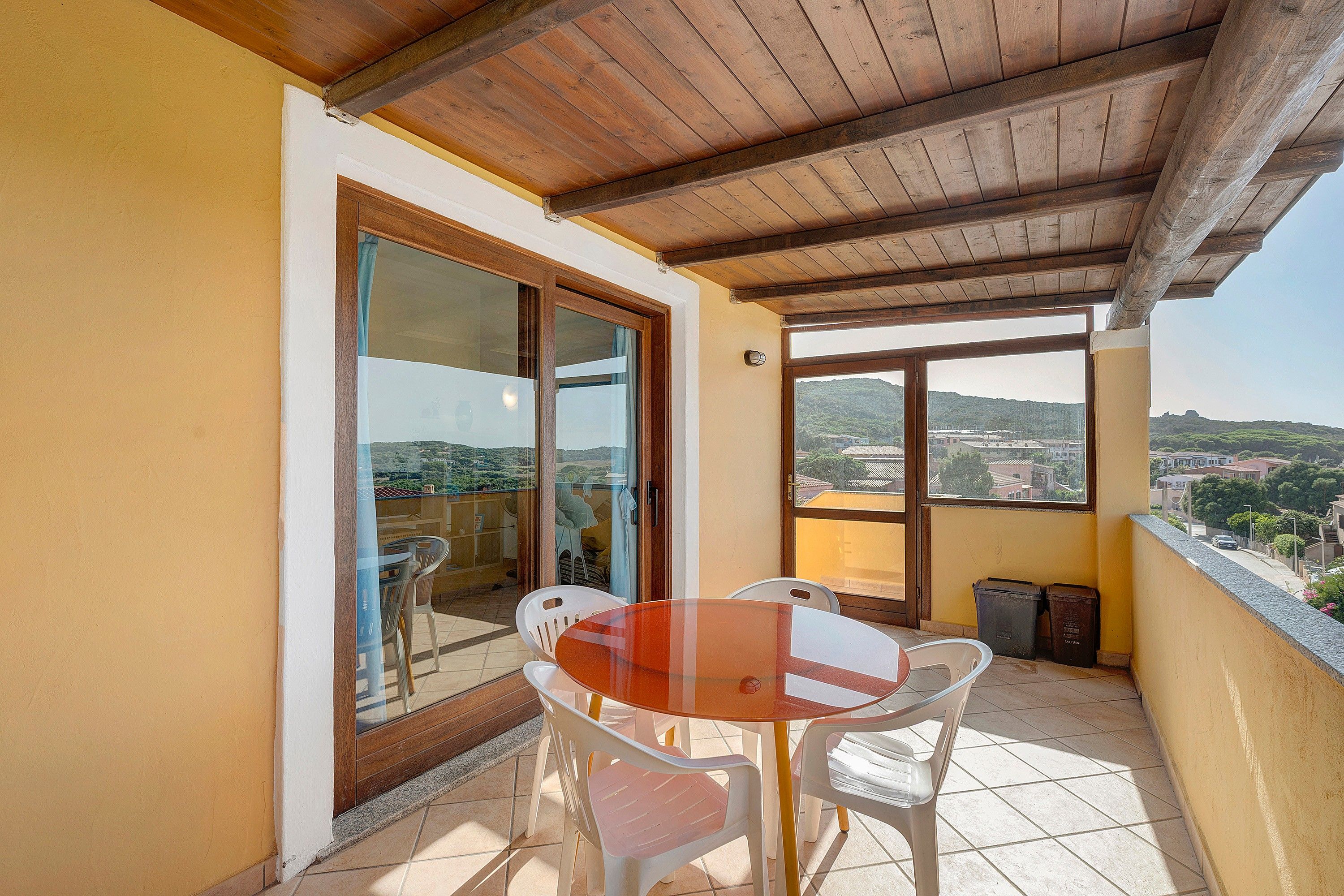 A balcony with a table and chairs, a view of the city, and a wooden ceiling.