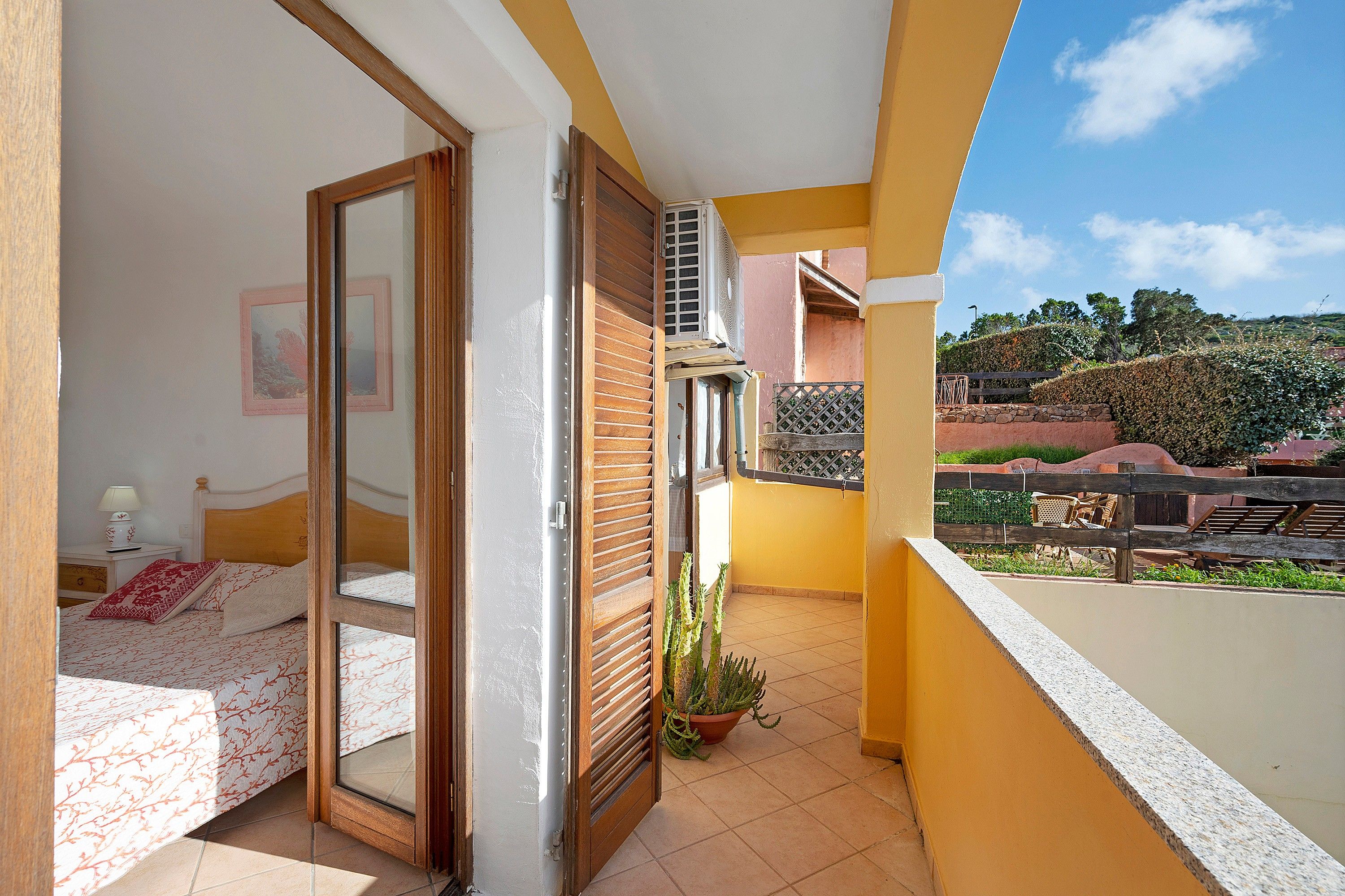 A balcony with a view of a hillside, a sliding door leading to a bedroom, and a potted plant.