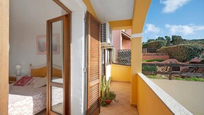 Un balcon donnant sur une colline, une porte coulissante menant à une chambre à coucher et une plante en pot.