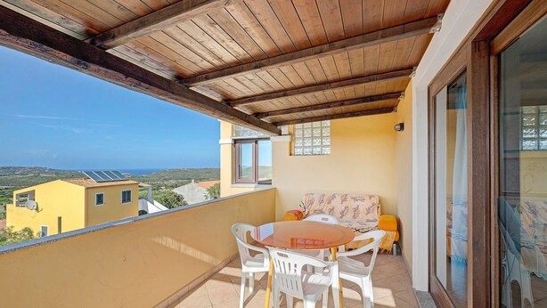 Un balcon doté d’un plafond en bois, une table avec des chaises, un canapé et une vue sur la mer et les bâtiments.