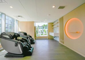 A modern spa room with massage chairs, a reception desk, and a view of buildings outside.