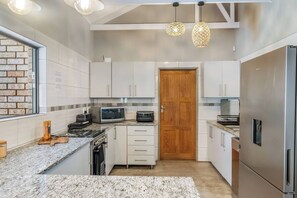 A modern kitchen with white cabinets, a granite countertop, a built-in oven, a microwave, and a refrigerator. - Kruger Villa - Where luxury meets nature (Marloth Park)