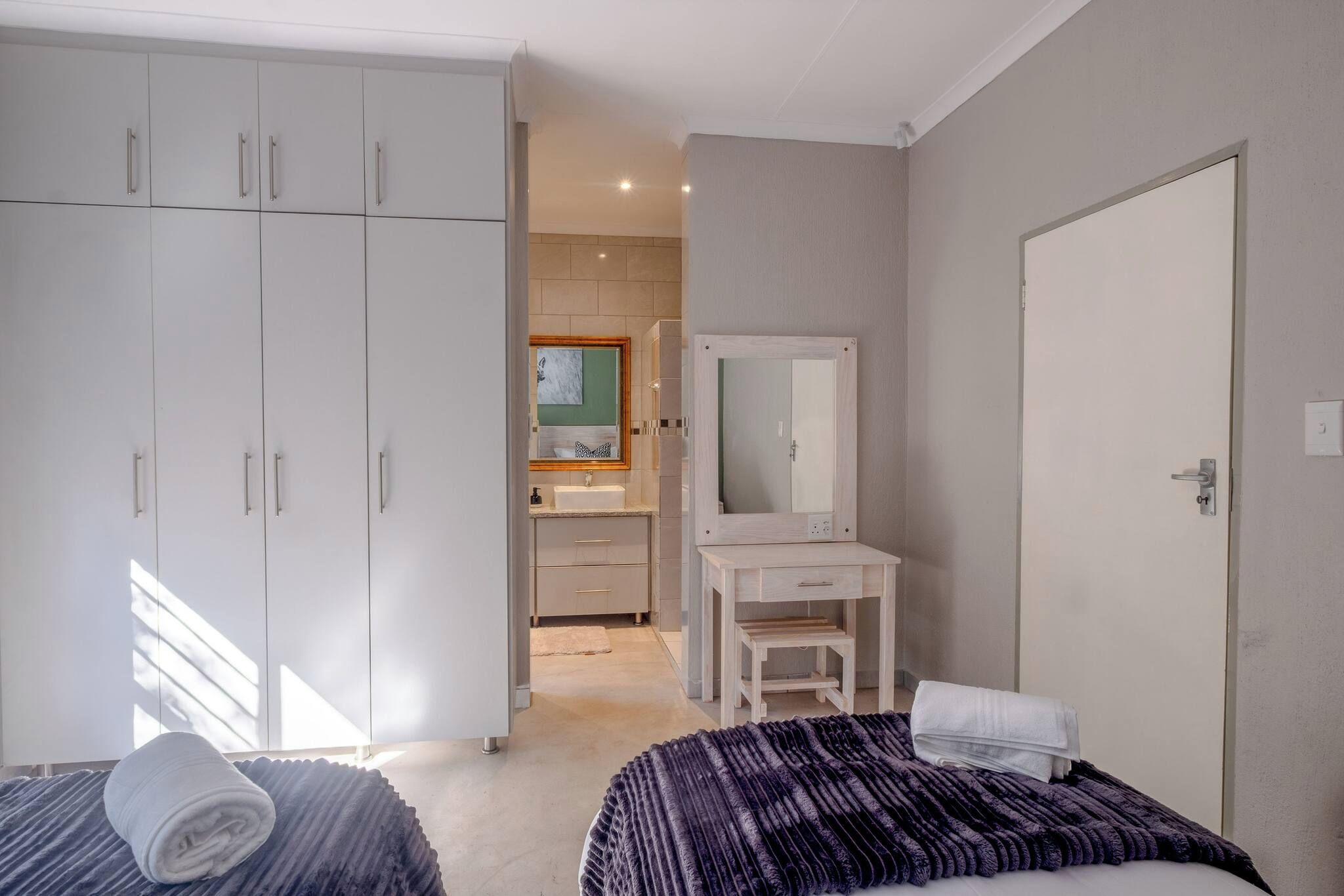 Un dormitorio con dos camas, un armario, un tocador y un baño visible al fondo.
