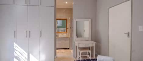 A bedroom with two beds, a wardrobe, a dressing table, and a bathroom visible in the background.
