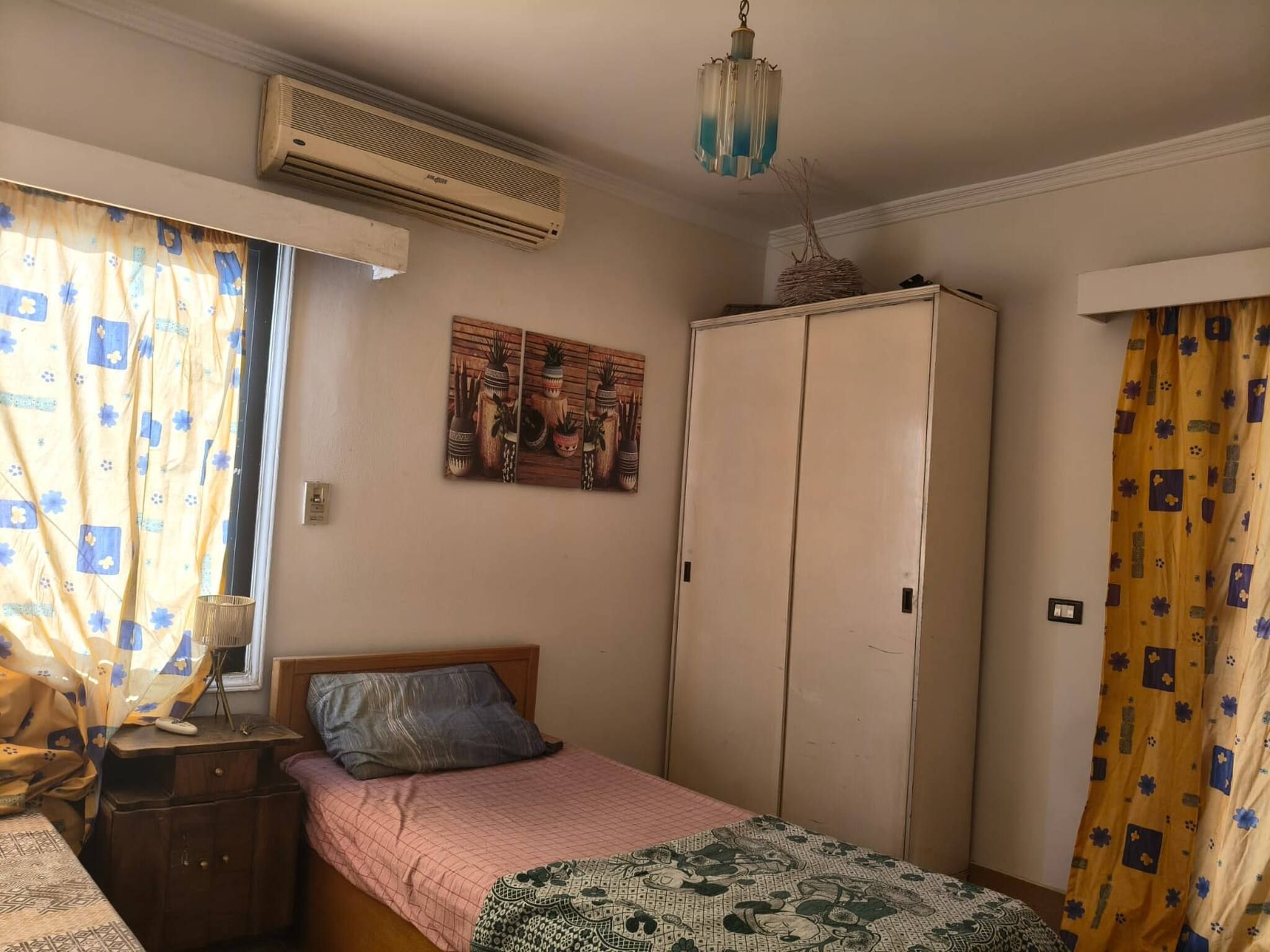 Un dormitorio con cama, armario, un cuadro y equipo de aire acondicionado.