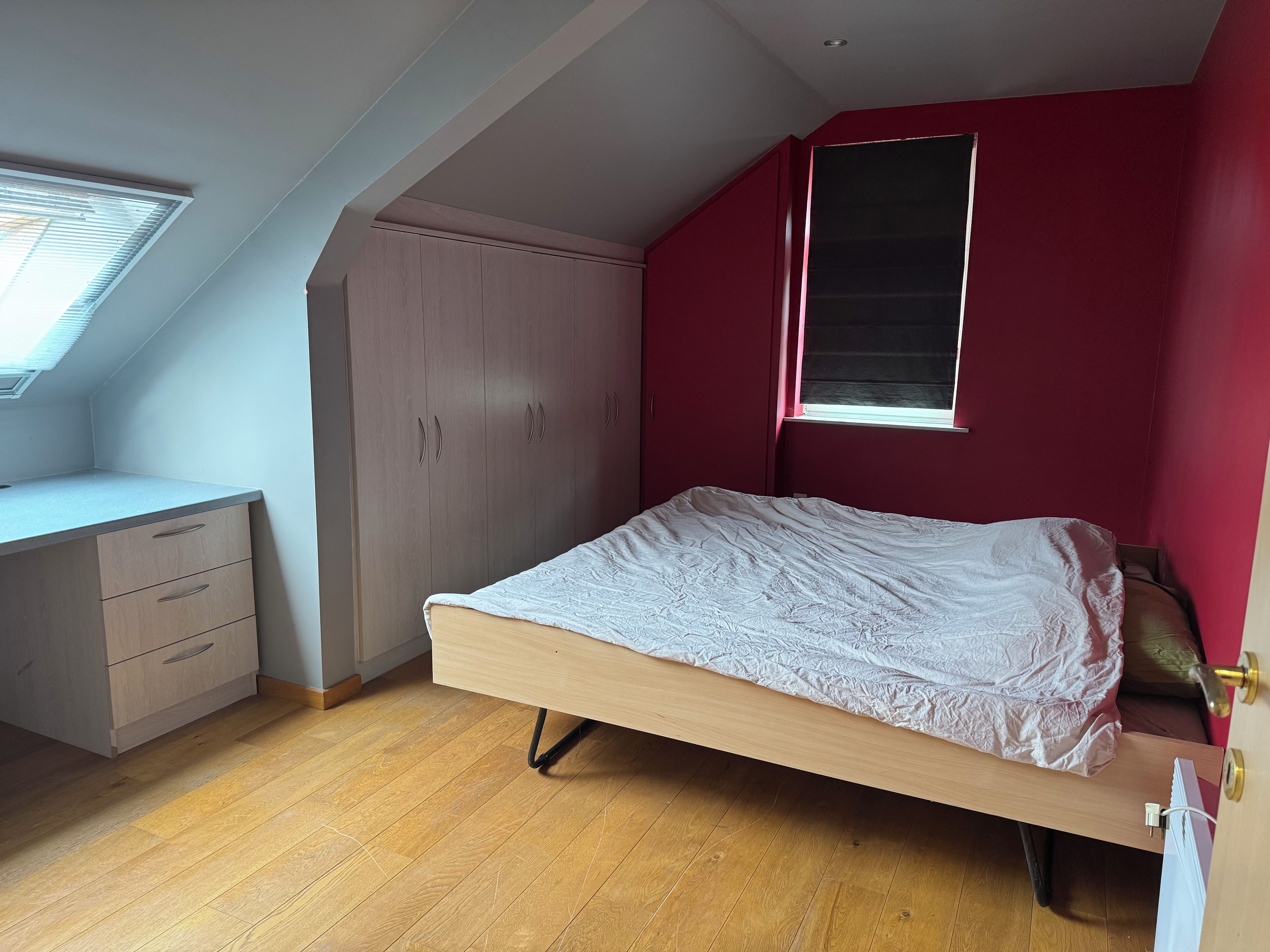 Un dormitorio con techo inclinado, una cama, un escritorio y un armario.