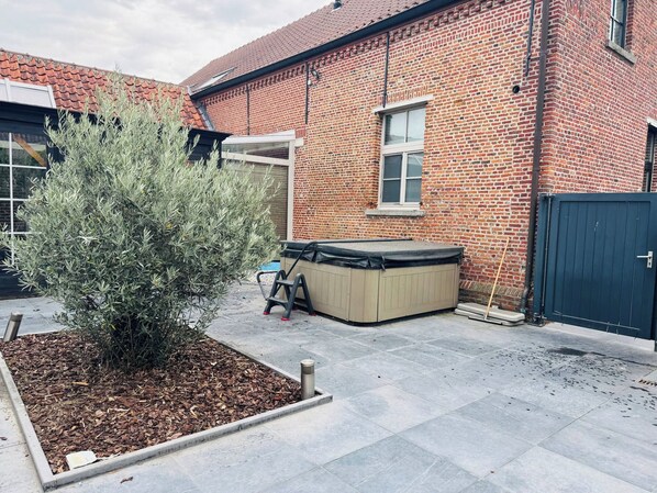 A brick building with a small garden area, a hot tub, and a black gate.