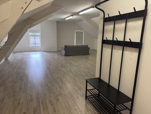 A spacious attic room with a sloped ceiling, a grey sofa, a black metal bench, and a wall-mounted rack.