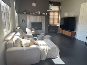 Ein modernes Wohnzimmer mit Kamin, Sofa, Fernseher und einem großen Fenster.