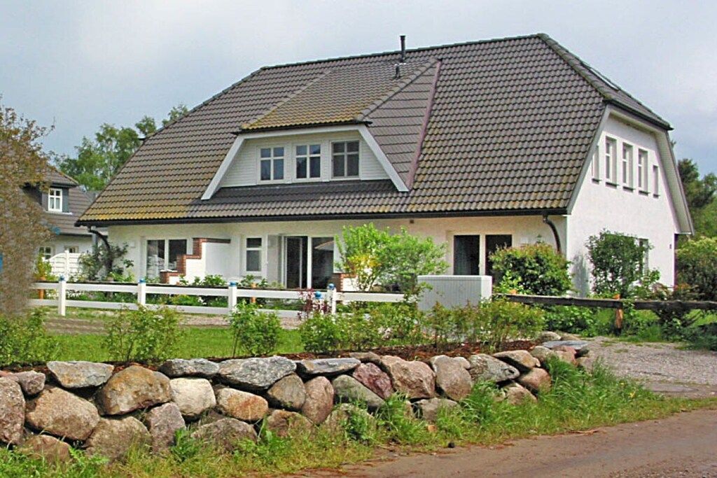 Une maison à deux étages, avec un mur de pierre à l’avant, une clôture blanche et une allée gravillonnée.