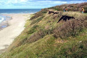 Eine Küstenlandschaft mit Strand, grasbewachsenen Klippen und einigen Spaziergängern.