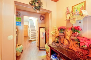A hallway with a wooden staircase, a wall decorated with various items including a wreath, and a table with potted plants and a bicycle.