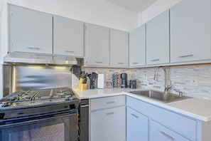 A modern kitchen with stainless steel appliances, white cabinetry, and a tiled backsplash.